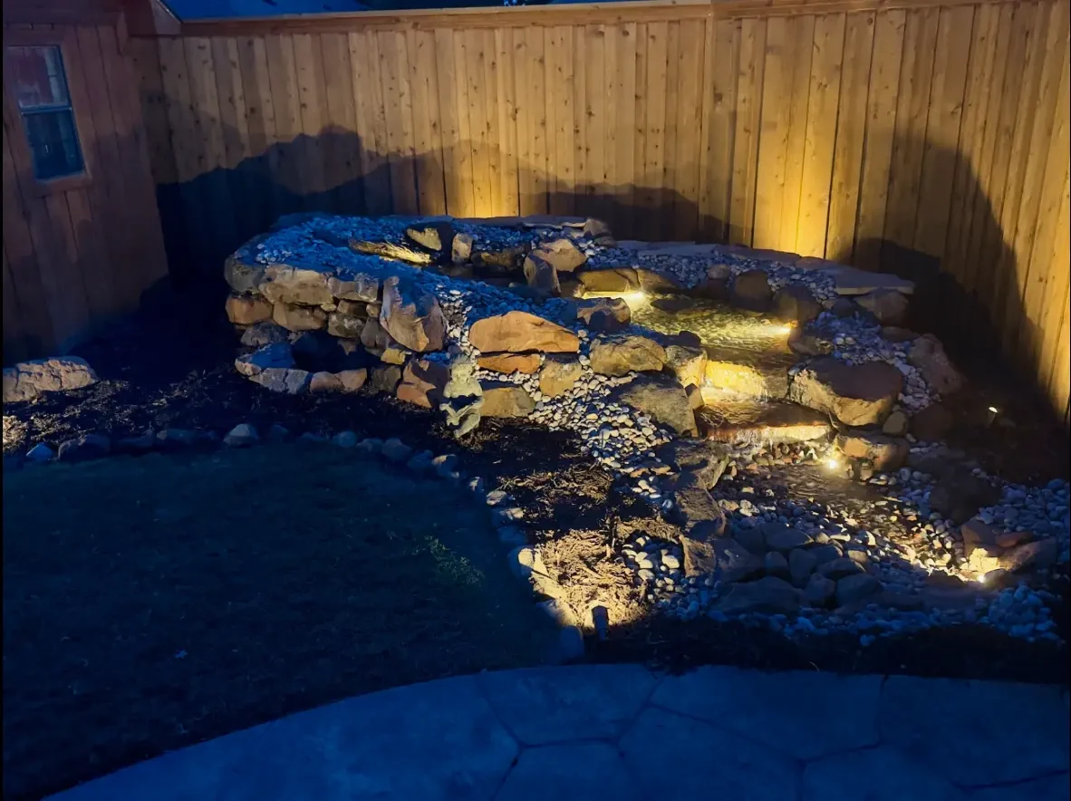 Backyard waterfall illuminated by warm landscape lights at dusk